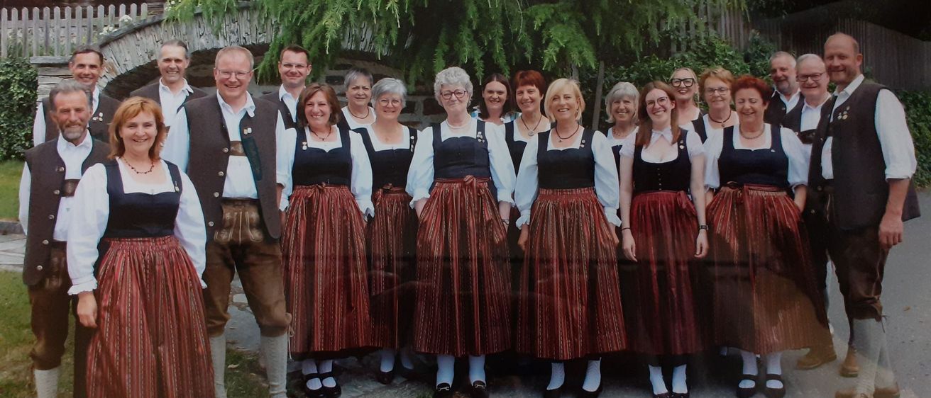 Eine Gruppe von Menschen in traditioneller Kleidung steht zusammen auf einem Bürgersteig vor Bäumen.