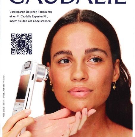 Das Cover einer Zeitschrift zeigt eine Frau, die ihre Haut mit einem Dermatoskop untersucht. Oben steht 'CAUDALIE'. Ein QR-Code ist oben links sichtbar.