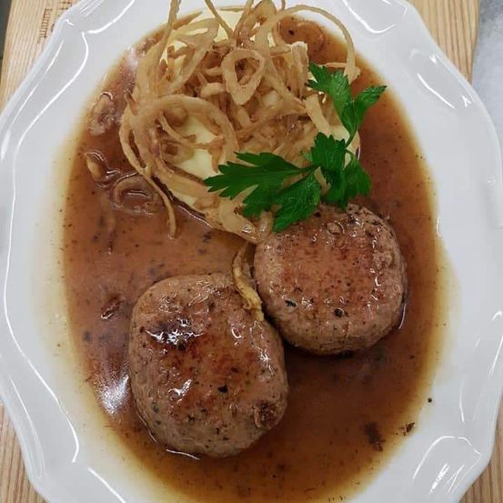 Ein Teller mit Fleischbällchen in brauner Sauce, gekrönt mit Petersilie und gebratenen Zwiebeln.