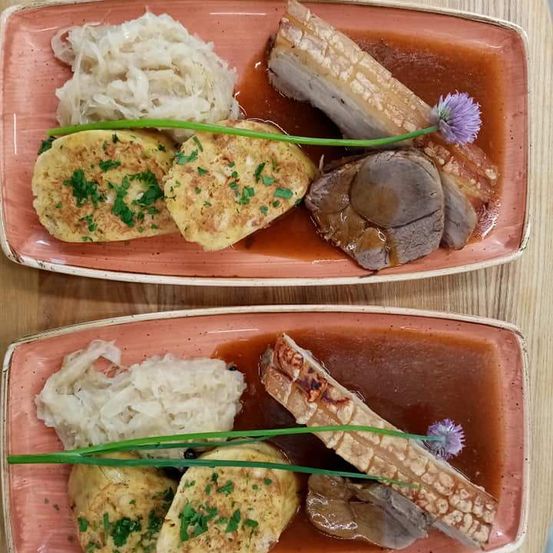 Zwei Teller mit Essen, jeder mit gebratenen Kartoffeln, Sauerkraut und einem Stück Fleisch in roter Sauce.