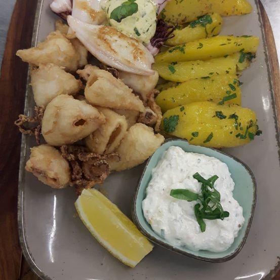 Ein Teller mit gebratenem Calamari, gelben Kartoffeln und eine Schüssel Dip-Sauce mit einer Zitronenscheibe.