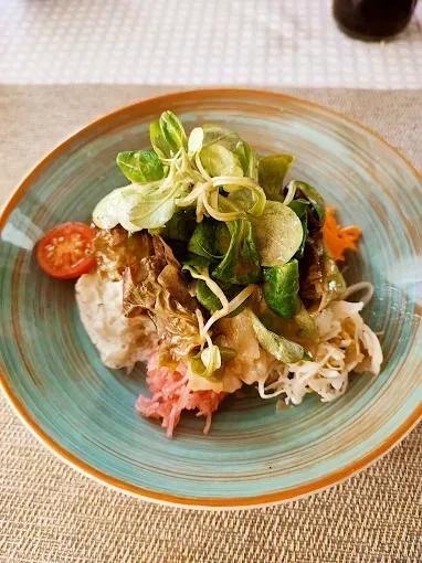Ein Salatgericht in einem blauen Teller mit goldenem Rand, bestehend aus Salat, Tomate und verschiedenen Gemüsesorten.