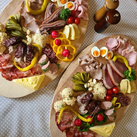 Zwei Holzbretter zeigen eine Charcuterieplatte mit geschnittenem Fleisch, Käse, Gurken und Gemüse. Verschiedene Wurstsorten, Schinken und Käse sind mit Tomaten und Radieschen angeordnet.