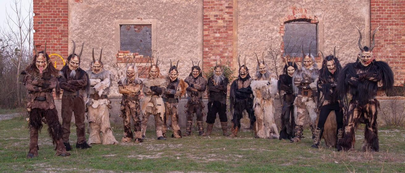 Eine Gruppe von Menschen in gehörnten Kostümen steht vor einem Backsteingebäude. Sie posieren für ein Foto.