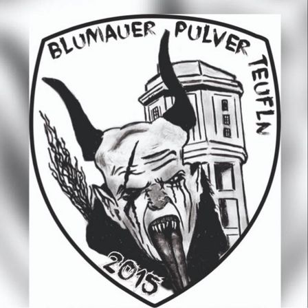 Eine Schwarz-Weiß-Zeichnung eines gehörnten Dämonengesichts mit 'Blumauer Pulver Teufeln 2015' darum herum. Das Gebäude hinter dem Dämon ist hoch und hat viele Fenster.