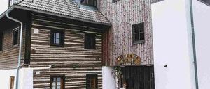 Ein Holzhaus mit mehreren Fenstern und einem kleinen Tor, umgeben von einem Holzzaun und einem Mülleimer.