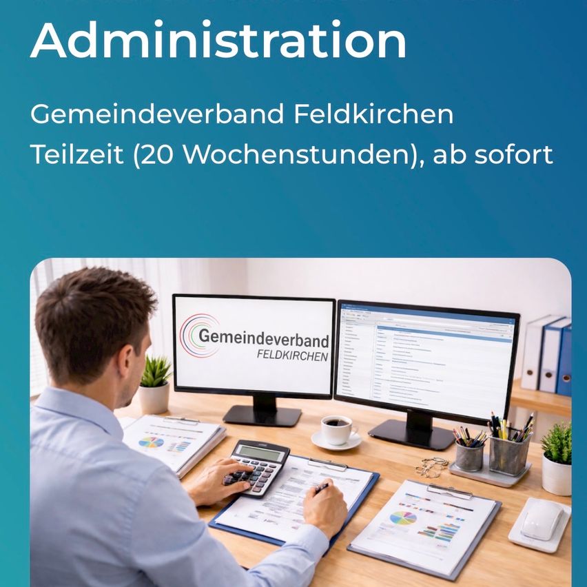 Ein Mann arbeitet an einem Schreibtisch mit zwei Computerbildschirmen, die den Text 'Gemeindeverband Feldkirchen' anzeigen. Der Schreibtisch ist mit Papieren, einem Becher, Stiften und einer Topfpflanze übersät.