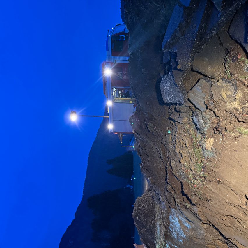 Eine Nachtszene zeigt ein Fahrzeug mit eingeschalteten Scheinwerfern, das am Rande eines steilen, felsigen Abgrunds positioniert ist. Die Scheinwerfer des Fahrzeugs beleuchten das raue Gelände darunter.