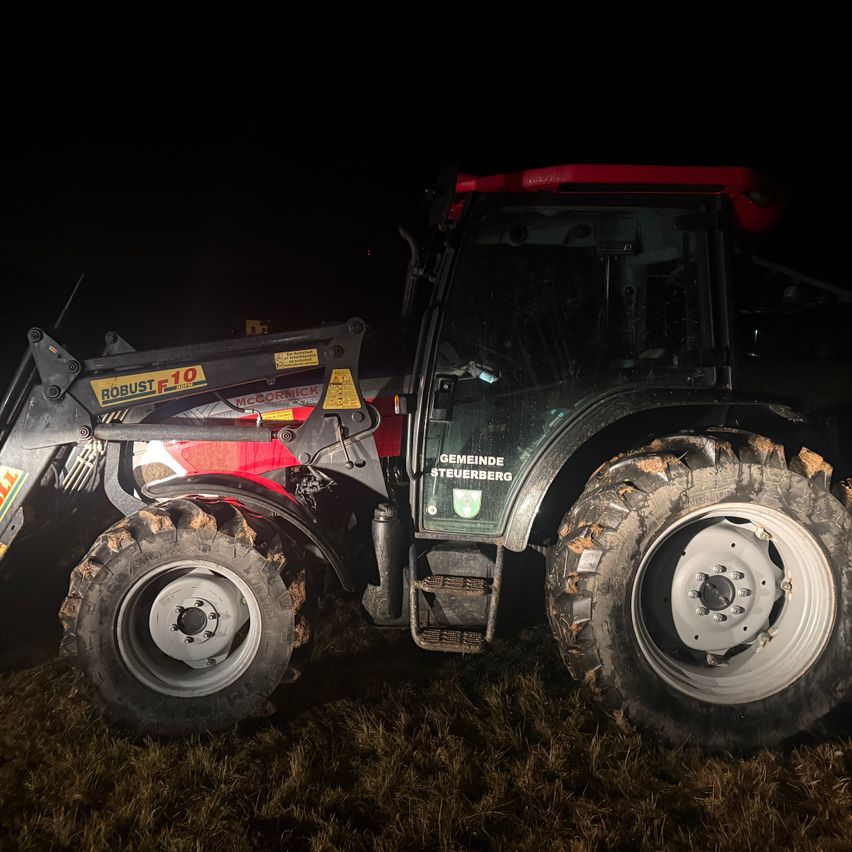 Ein roter Traktor mit der Aufschrift 'Robust F10' und 'Gemeinde Steuerberg' steht nachts auf einem Feld.