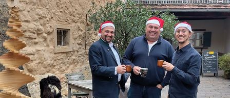 Werbeposter für die Weihnachtsveranstaltung im Saxxes Passage mit drei Männern in Weihnachtsmützen, die Tassen halten, und einer spiralförmigen Holzskulptur. Die Veranstaltung läuft vom 25. November bis 18. Dezember 2025. Dienstag, Mittwoch und Donnerstag von 16-22 Uhr geöffnet.