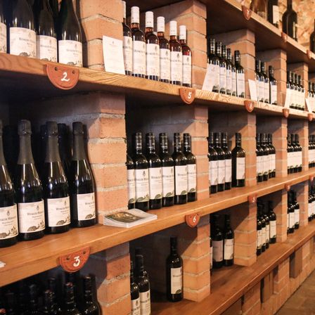 Ein Holzregal mit mehreren Reihen von Weinflaschen in einem Weinladen, mit Nummernschildern, die verschiedene Bereiche kennzeichnen.