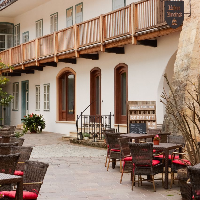 A cozy outdoor seating area of a restaurant with wooden tables and chairs, a balcony, and a signboard.
