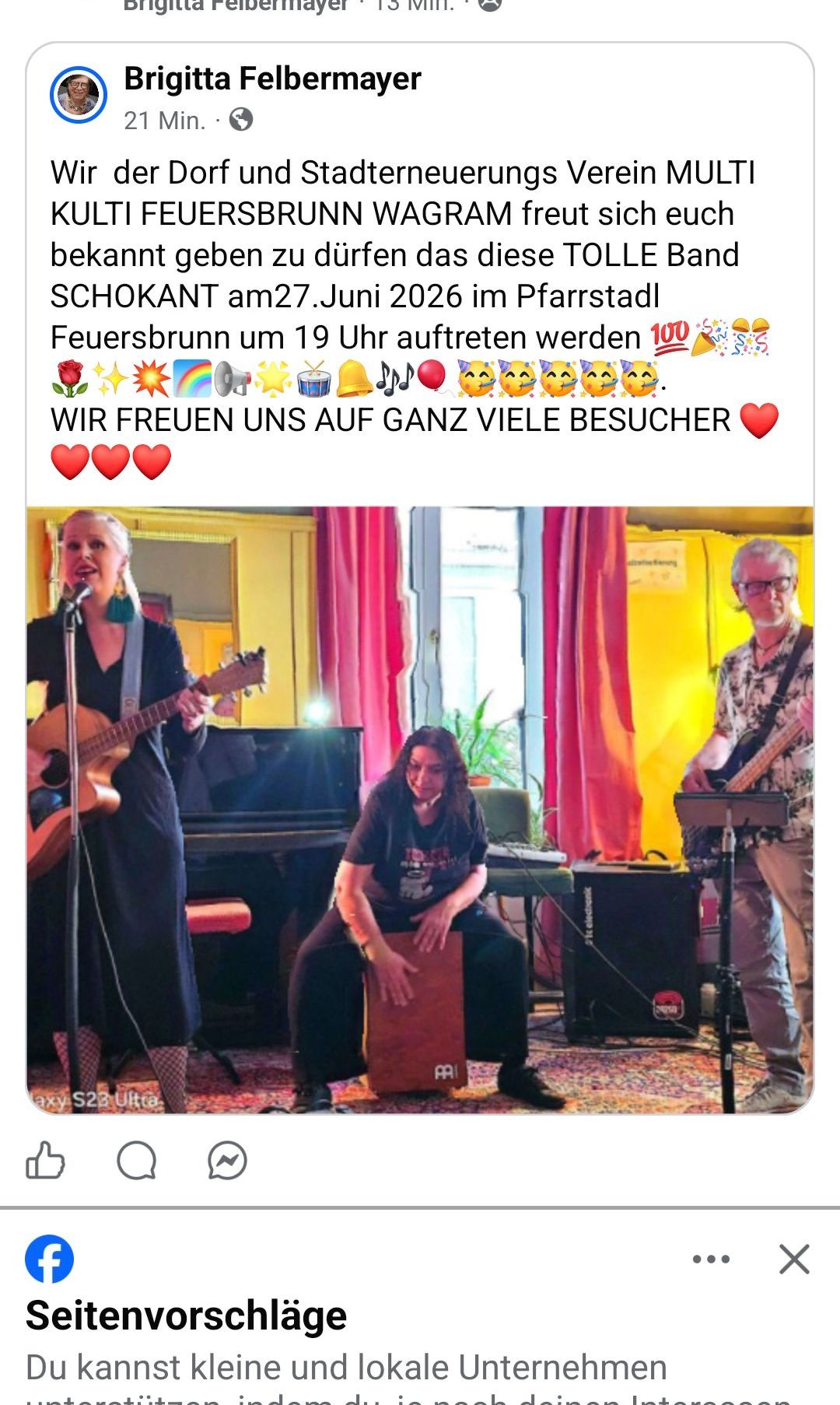 A band with a woman playing guitar, a man on percussion, and another man with a guitar. They are performing at a venue with a piano and a drum set.