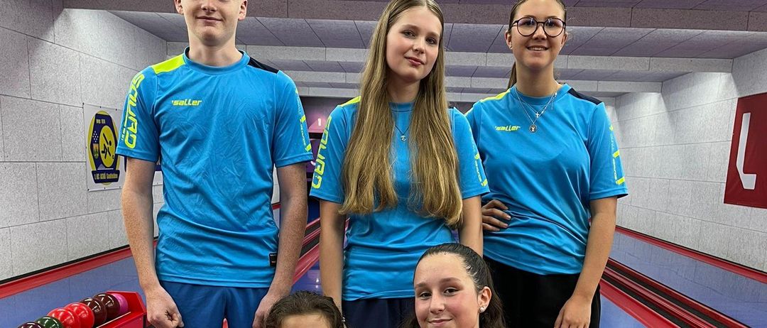 Eine Gruppe von fünf Personen, möglicherweise Teamkollegen, in passenden blauen und gelben Trikots, steht und posiert für ein Foto in einer Bowlingbahn.