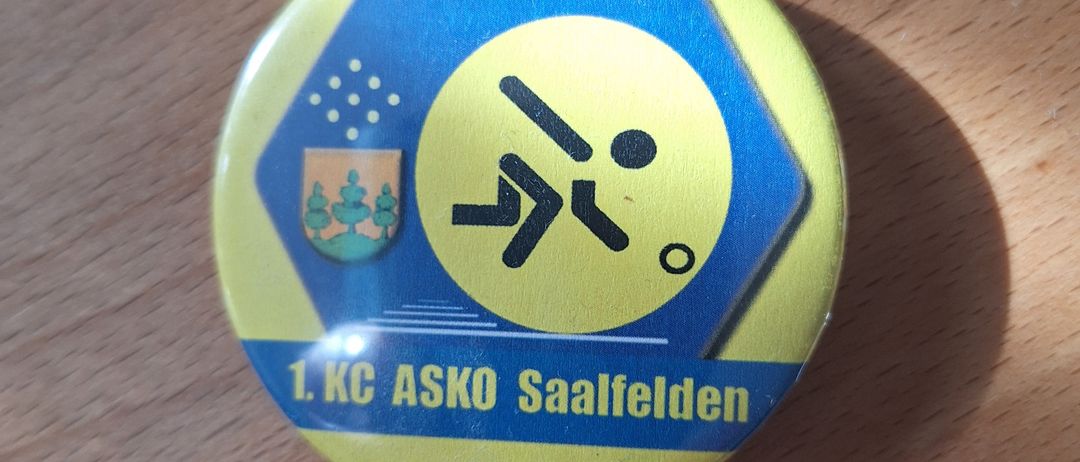 Ein gelber und blauer Abzeichen, gegründet 1974, zeigt eine laufende Figur und den Text '1. KC ASKO Saalfelden'.