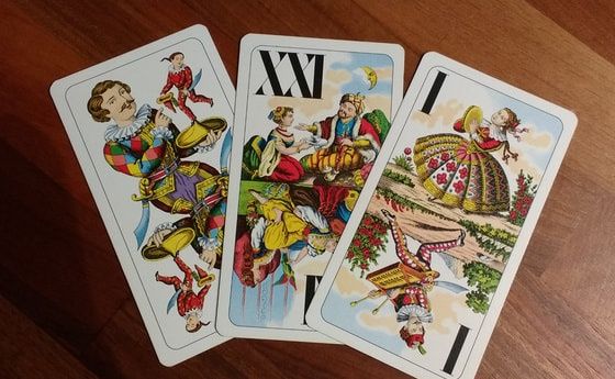 Drei Karten liegen auf einer Holzoberfläche. Eine Karte zeigt einen Mann mit einem Schwert, eine andere zeigt ein Paar mit römischen Ziffern XII und die dritte zeigt eine Frau in einem roten Kleid.