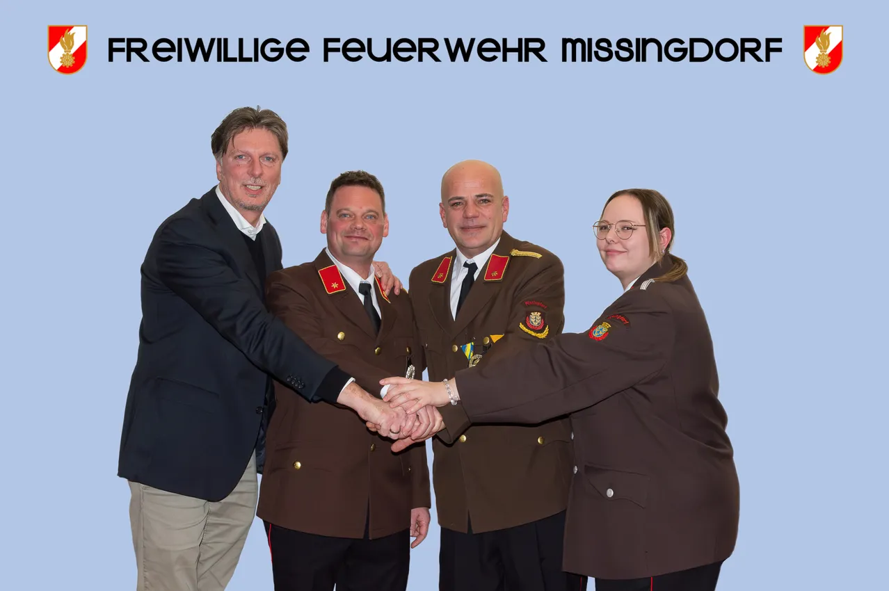 Vier Personen stehen zusammen und schütteln Hände. Sie tragen Uniformen mit dem Text 'Feuerwehr' und 'MissingDon'. Über ihnen ist ein blauer Hintergrund mit weißem Text.