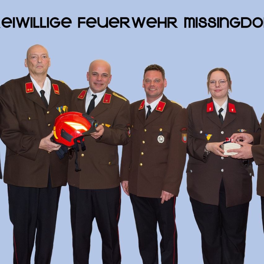 Fünf Personen in Uniformen stehen vor einem blauen Hintergrund. Sie halten einen Helm und eine Medaille. Die Worte Freiwillige Feuerwehr Missingdorf sind oben geschrieben.