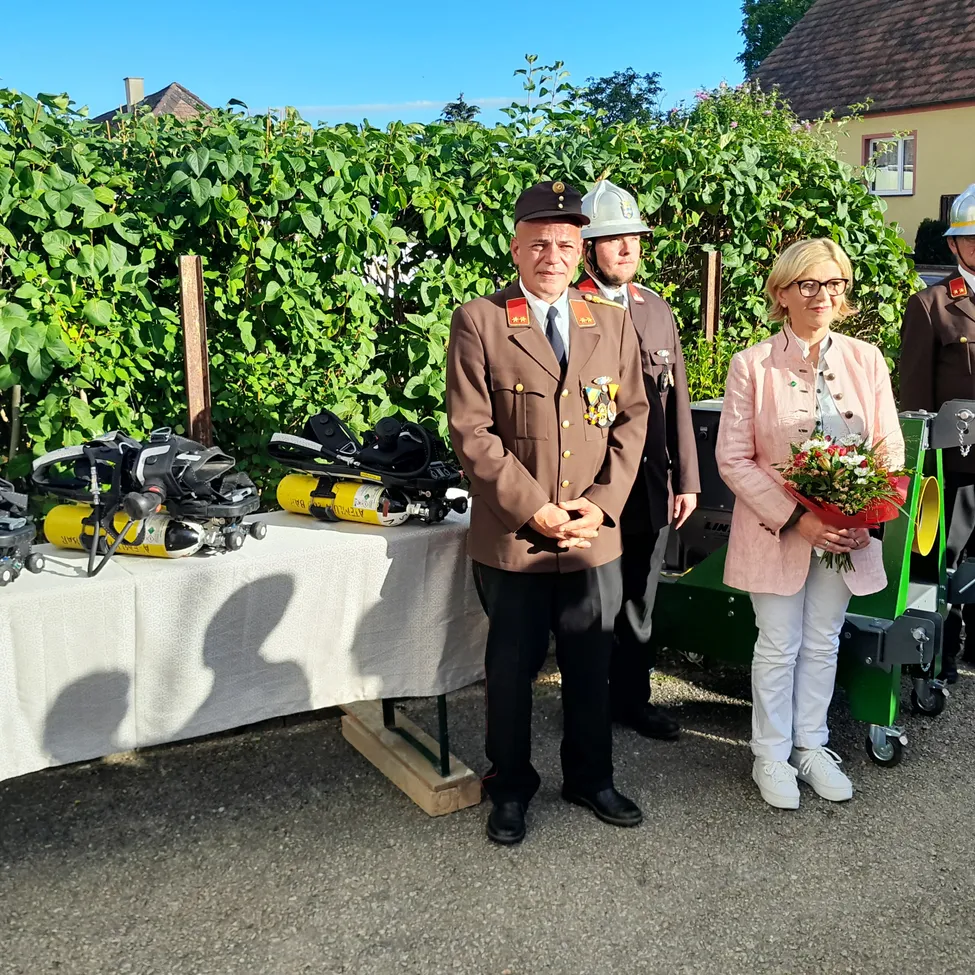 Ein Mann und eine Frau stehen vor einem Tisch mit Ausrüstung, dahinter stehen zwei Männer in Uniform.