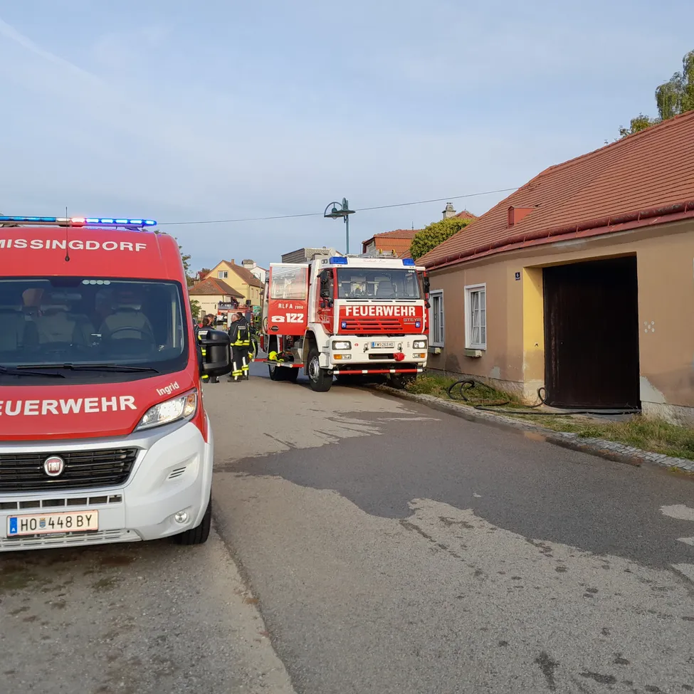 Ein roter und weißer Feuerwehrwagen ist am Straßenrand geparkt, vor ihm steht ein Polizeiwagen.