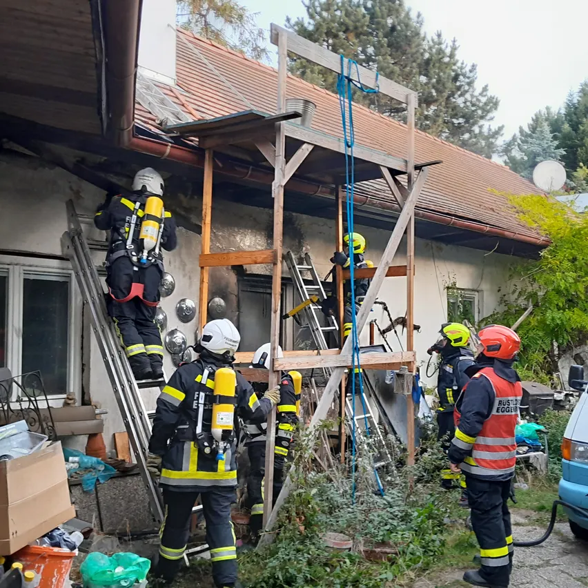 Eine Gruppe von Feuerwehrleuten arbeitet an einem Haus mit beschädigtem Dach.