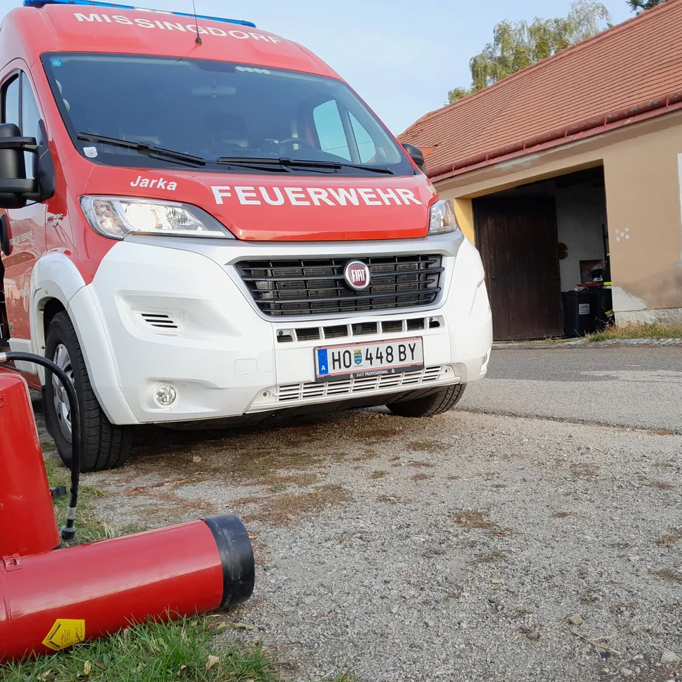 Ein roter und weißer Feuerwehrwagen ist am Straßenrand geparkt, die Tür steht offen und ein Feuerlöscher liegt auf dem Boden.