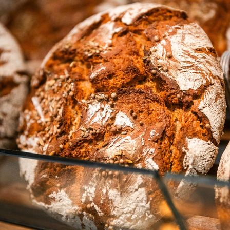 Eine Nahaufnahme eines runden, goldbraunen Brotes mit Samen darauf, präsentiert in einer Glasvitrine.