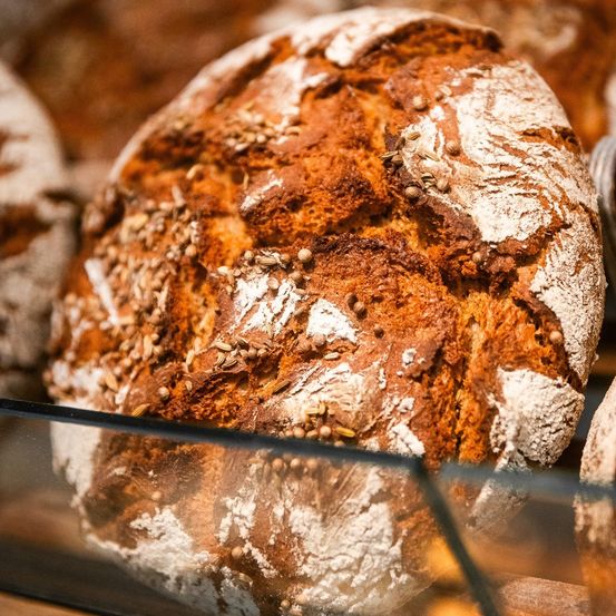 Eine Nahaufnahme eines runden, goldbraunen Brotes mit Samen darauf, präsentiert in einer Glasvitrine.