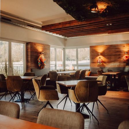 Ein leeres Restaurant mit Holztischen und -stühlen, Holzwänden und großen Fenstern mit Blick nach draußen.