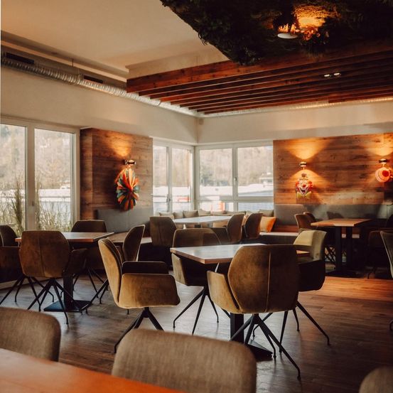 Ein leeres Restaurant mit Holztischen und -stühlen, Holzwänden und großen Fenstern mit Blick nach draußen.