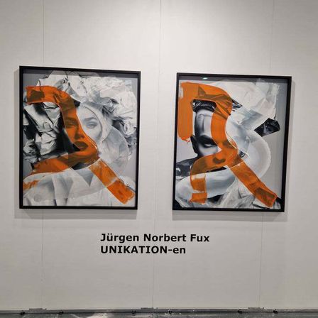 Zwei abstrakte Gemälde von Jürgen Norbert Fux sind an einer weißen Wand ausgestellt. Die Gemälde zeigen ein Gesicht mit kräftigen orangefarbenen Linien. Unter den Gemälden stehen der Name des Künstlers und der Titel 'UNIKATION-en'.