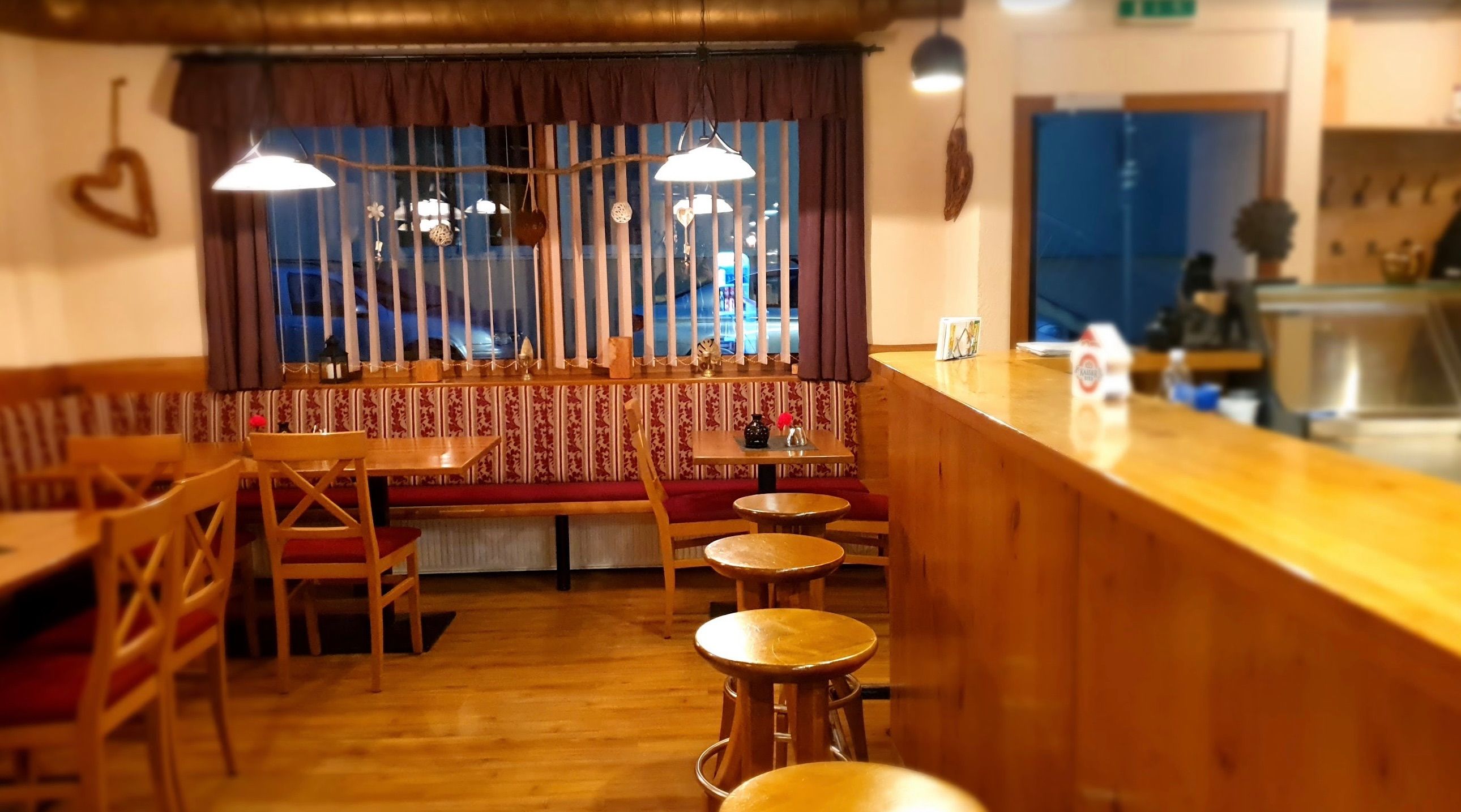 Ein Innencafe mit Holzmöbeln, einer roten gepolsterten Bank, einer Bartheke und einem Fenster mit Jalousien.