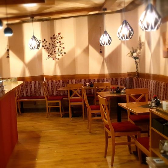 Ein Restaurant mit Holzboden, das mehrere Tische und Stühle bietet. Die Wände sind mit dekorativen Lichtern und Kunst geschmückt. Die Atmosphäre ist warm mit einem roten Thema.
