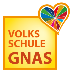Ein gelbes Schild mit einem bunten Herz darüber. Der Schriftzug 'VOLKSSCHULE GNAS' ist in roter und weißer Schrift geschrieben.