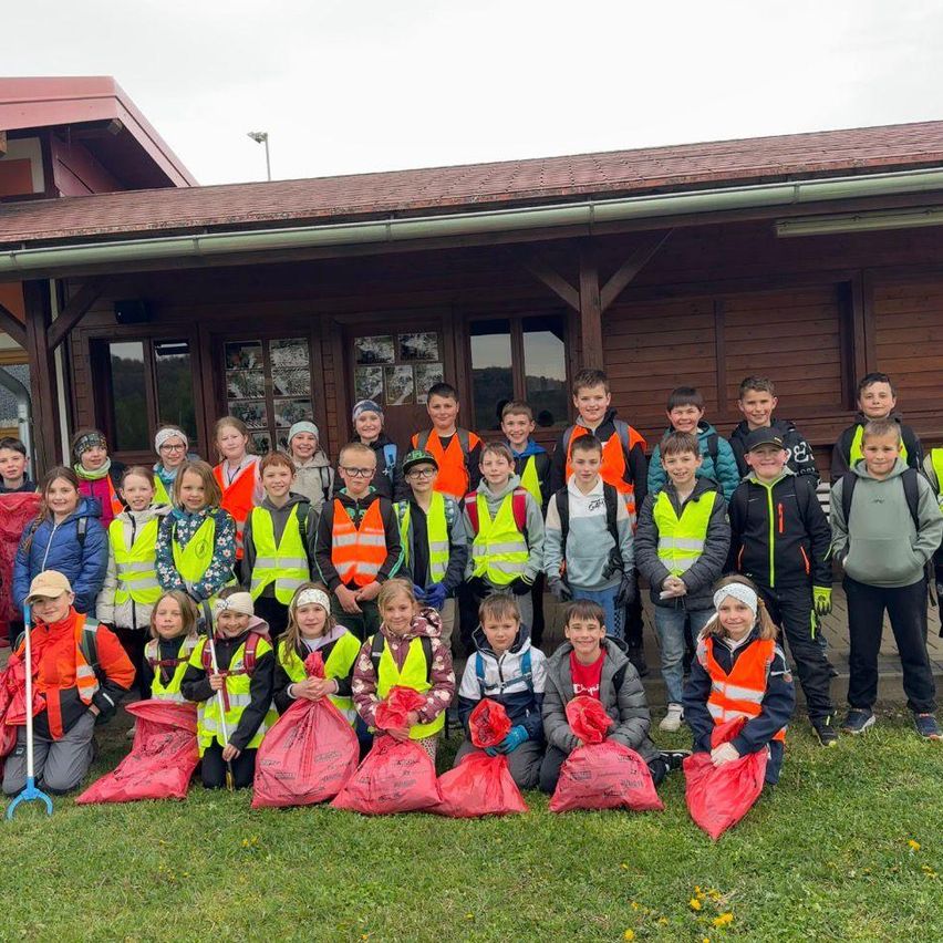 Eine Gruppe von Kindern in Sicherheitswesten posiert für ein Foto mit roten Müllsäcken vor einem Gebäude.