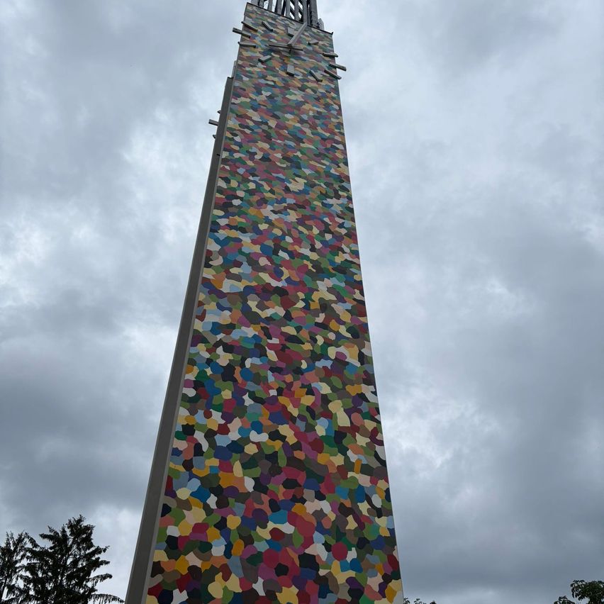 Ein hoher Turm mit einem farbenfrohen Mosaikdesign an einem bewölkten Tag. Der Turm hat eine Uhr nahe der Spitze.
