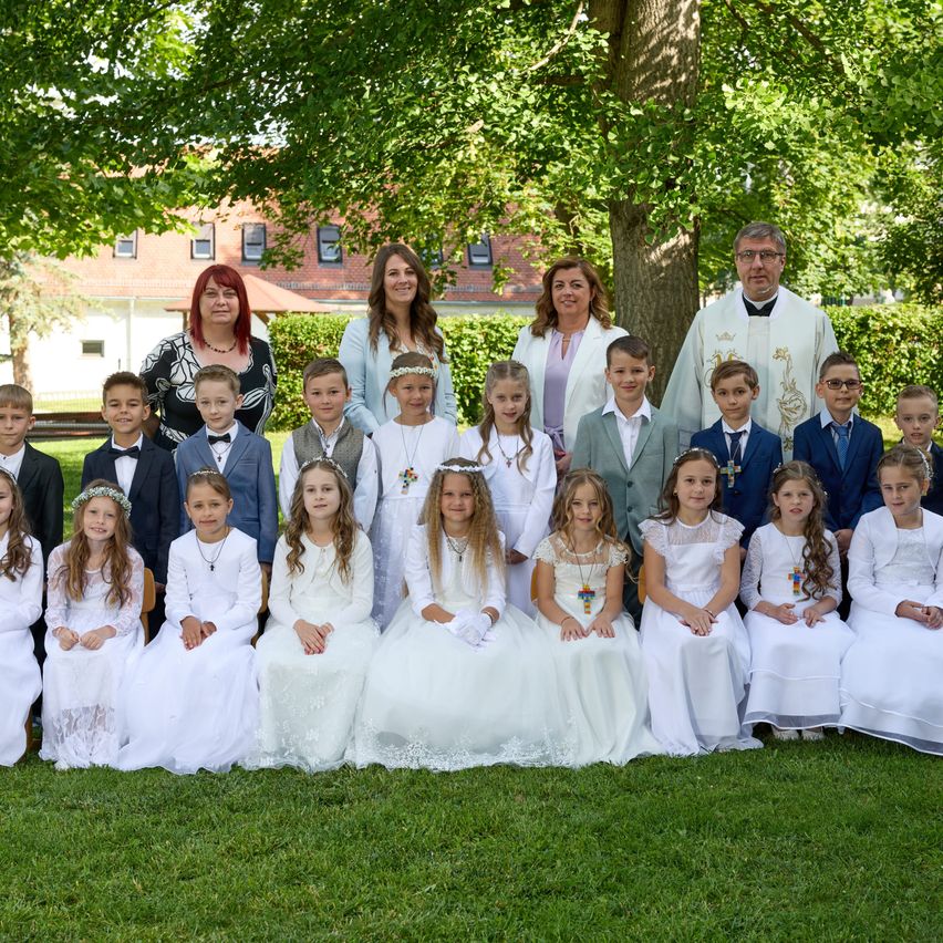Eine Gruppenaufnahme einer Kirchengemeinde mit Erwachsenen und Kindern in weißen Kleidern vor einem Baum und einem Gebäude.