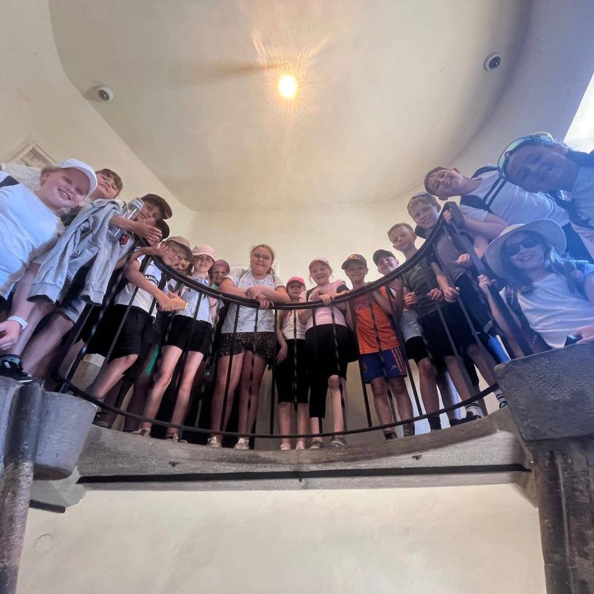 Eine Gruppe junger Menschen posiert für ein Foto auf einer Wendeltreppe mit Metallgeländern, einige tragen Hüte und Sonnenbrillen.