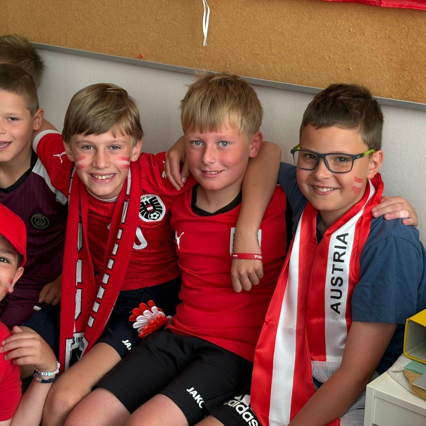 Fünf Jungen mit roten und weißen Kleidungsstücken mit dem Wort Österreich auf einem Schal, zusammen sitzend, zwei von ihnen mit Gesichtsbemalung.