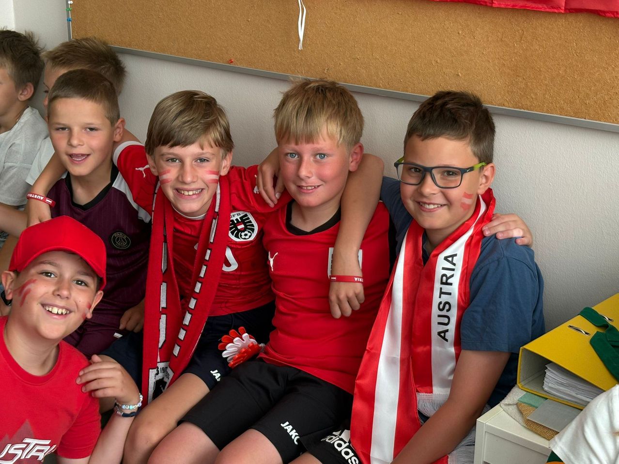 Fünf Jungen mit roten und weißen Kleidungsstücken mit dem Wort Österreich auf einem Schal, zusammen sitzend, zwei von ihnen mit Gesichtsbemalung.