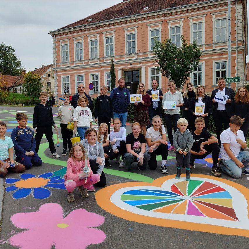 Eine Gruppe von Menschen posiert für ein Foto vor einem Gebäude mit einem farbenfrohen herzförmigen Design auf dem Boden.