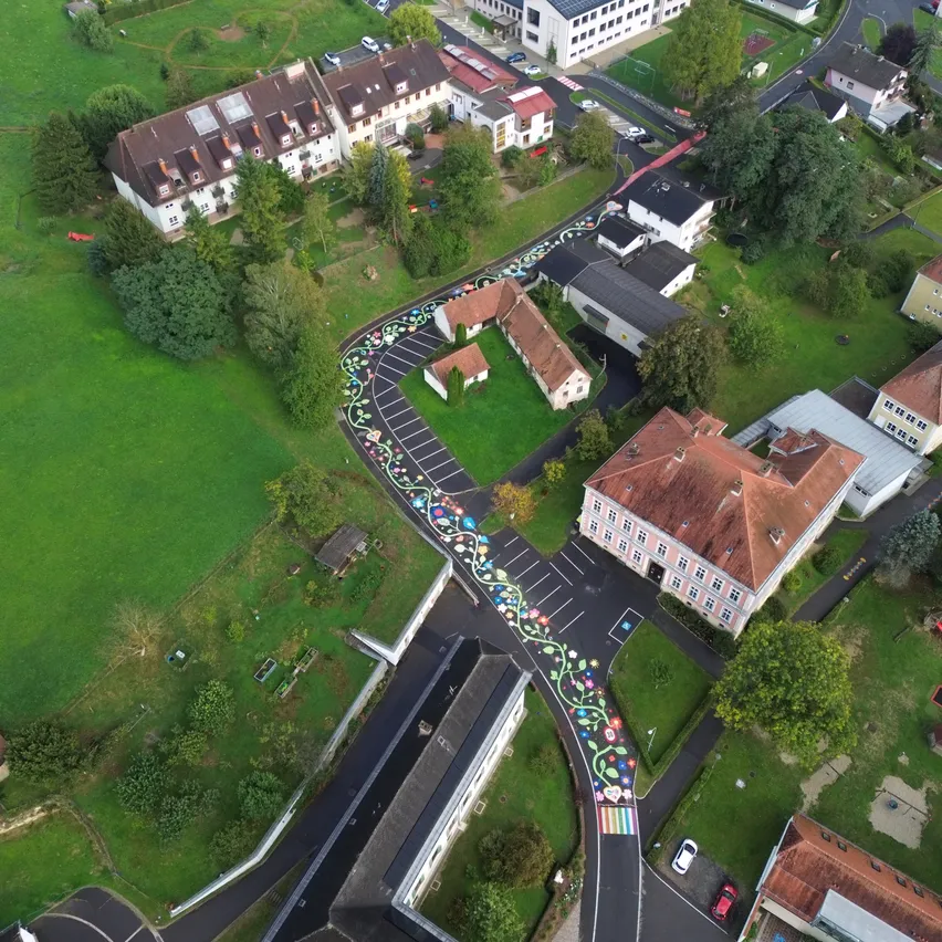Ein Luftbild eines Wohngebiets mit einem farbenfrohen Straßendesign. Die Straße ist mit Blumen verziert und hat ein Regenbogenmuster.