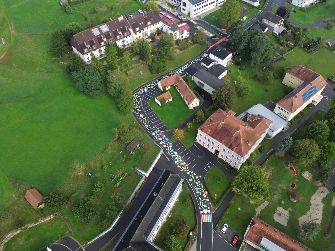 Ein Luftbild eines Wohngebiets mit einem farbenfrohen Straßendesign. Die Straße ist mit Blumen verziert und hat ein Regenbogenmuster.