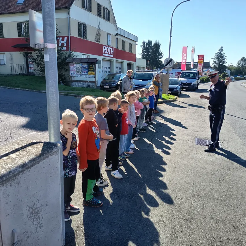 Eine Gruppe von Kindern steht in einer Reihe am Straßenrand, ein Polizist steht in der Nähe.
