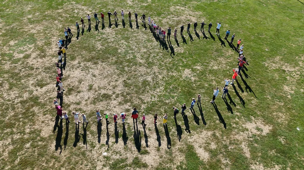 Eine Gruppe von Menschen steht in Herzform auf einem Grasfeld.