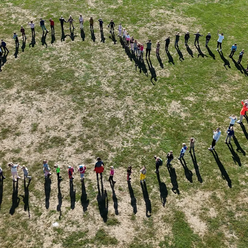 Eine Gruppe von Menschen steht in Herzform auf einem Grasfeld.