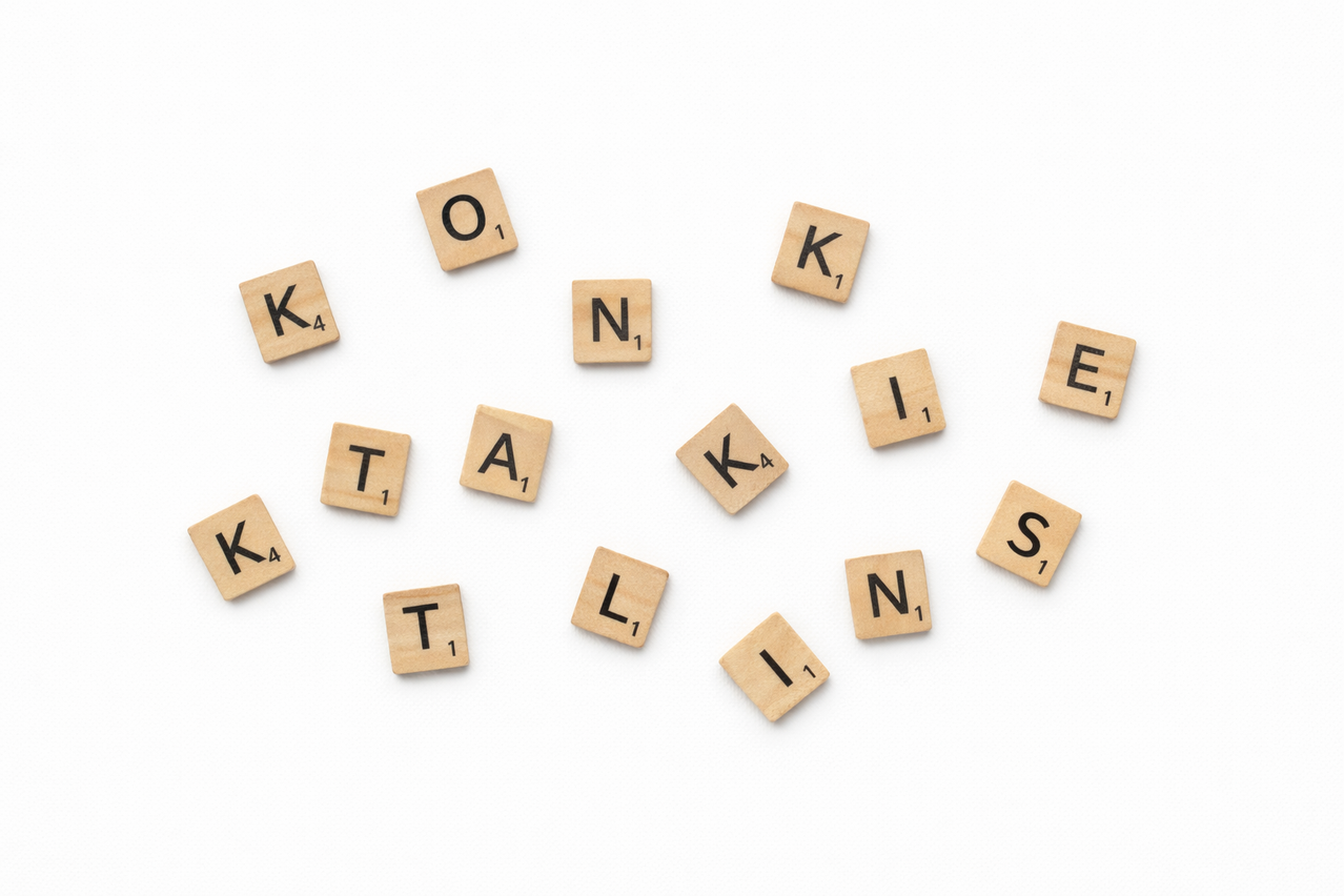 Eine Sammlung von hölzernen Scrabble-Steinen mit Buchstaben wie K, N, T und E, verstreut auf einem weißen Hintergrund. Jeder Stein hat einen schwarzen Buchstaben und eine Zahl, angeordnet in einem kreisförmigen Muster.