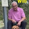 Ein Mann in einem rosa Hemd sitzt auf einem Felsen mit seinem Beagle. Das Foto hat die Namen 'Willi' und 'Anton' oben. Ein Schild in der Nähe steht 'Willi'.