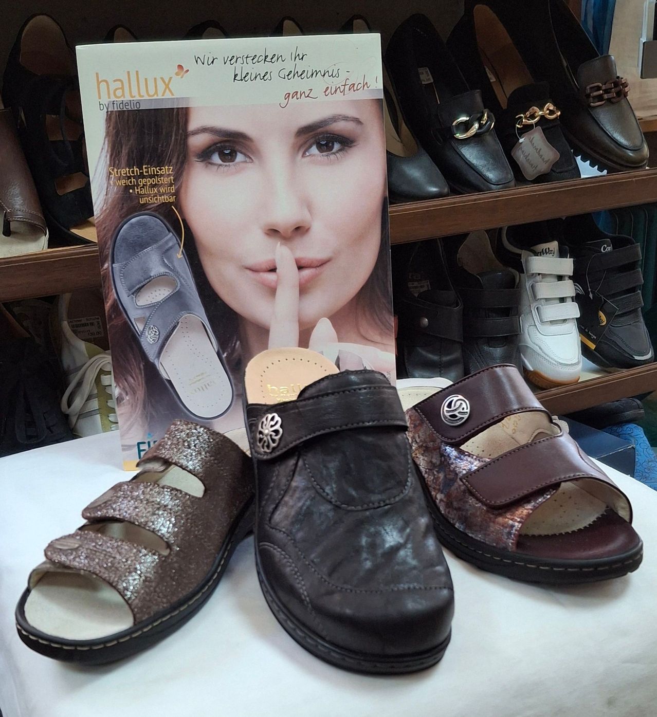 Eine Schuhausstellung mit braunen und glitzernden Sandalen auf einem weißen Tuch, begleitet von einem Zeitschriftencover mit einer Frau, die einen Finger über ihren Lippen hält.