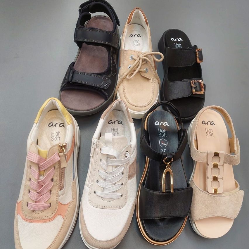 Sechs Paare Sandalen und Sneakers sind ausgestellt. Zwei Paare sind schwarz mit Schnallen, eines ist beige mit Schnürsenkeln und drei Paare sind hellbeige mit unterschiedlichen Designs und Farben.